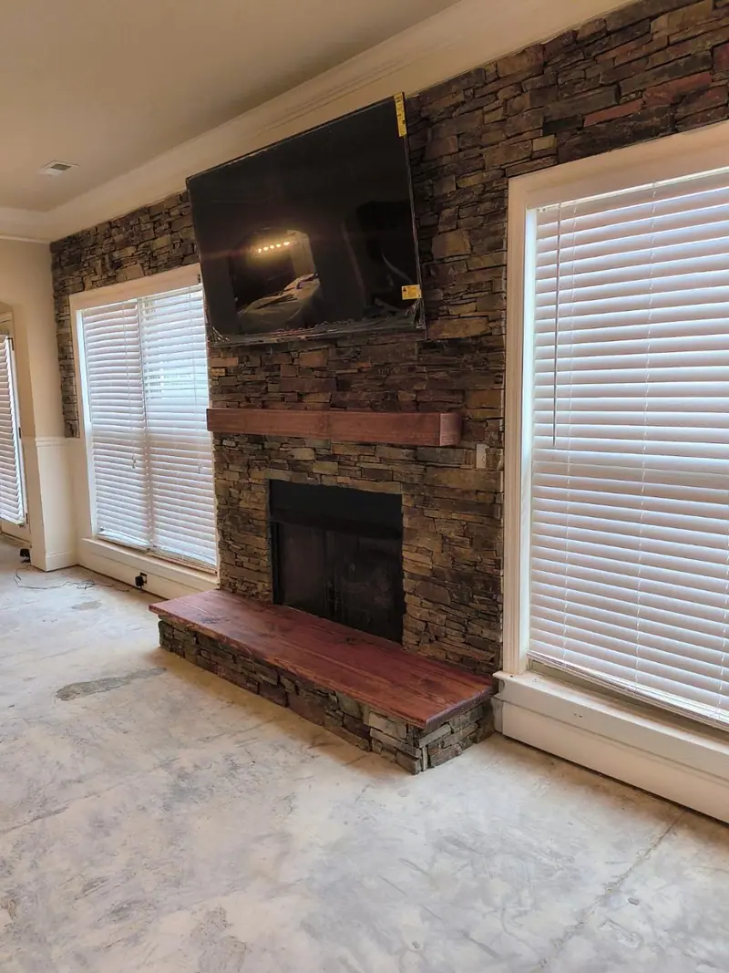 The same fireplace wall after, finished in stacked stone with a wood mantel